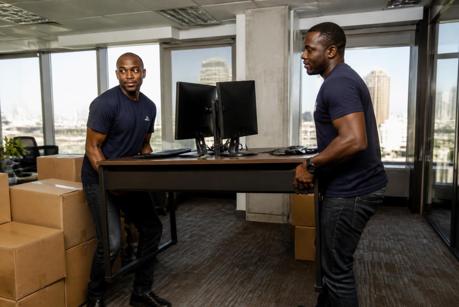 Kejani movers in blue branded t-shirts carrying an office desk and monitors during an office relocation in Nairobi